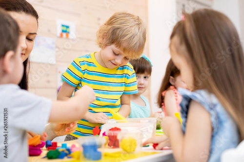 Children with teacher play colorful clay toy in daycare