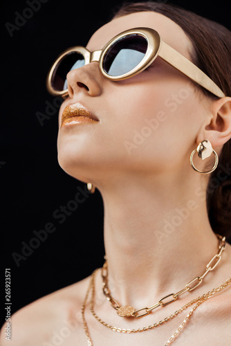 young attractive naked woman in sunglasses and golden jewelry isolated on black photo