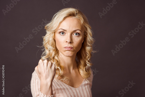 angry blonde woman looking at camera and showing fist isolated on black