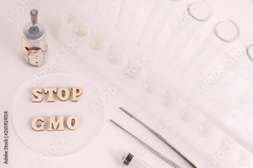 Wallpaper Mural Laboratory subjects: transparent petri dish, test tubes, flasks, nippers, syringe, tweezers. The phrase STOP GMO written in wooden letters. The concept of combating genetically modified products. Torontodigital.ca