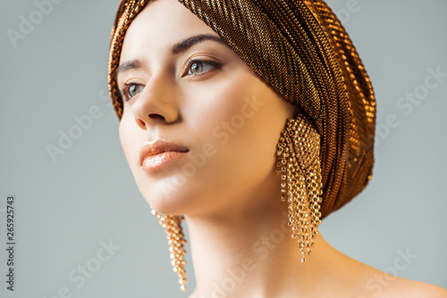 Fototapeta young naked woman with shiny makeup, golden rings in turban looking away isolate