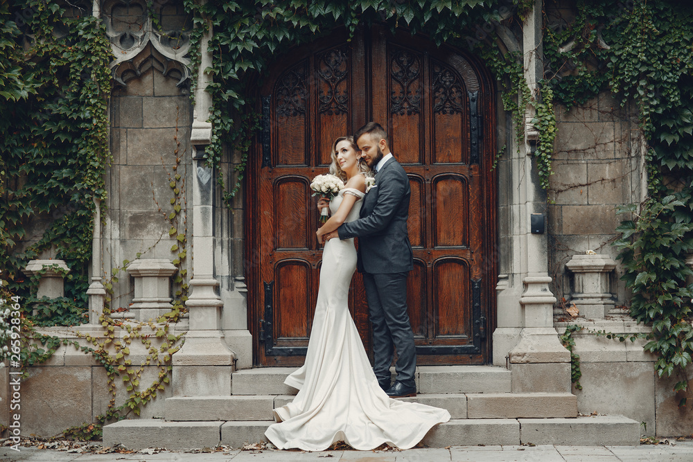 Beautiful bride in a long white dress. Handsome groom in a black suit. Couplenear old building.