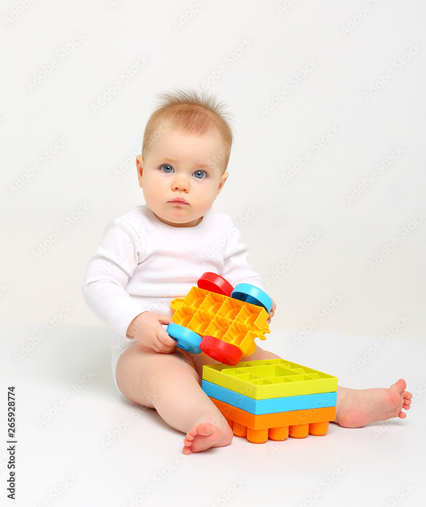 Charming blue-eyed baby sitting on a white background with colored educational toys Charming blue-eyed baby sitting on a white background with colored educational toys