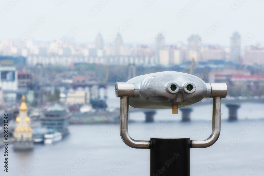 Coin operated electronic binocular for tourists on a blurred urban landscape