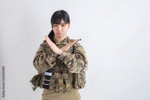 白背景に迷彩服の女の子が笑顔で手で不正解バツと表示しているサバイバルゲーム