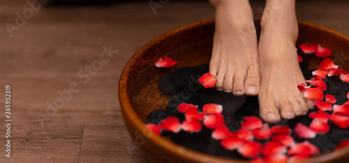 Closeup shot of a woman feet dipped in water with petals in a wooden bowl