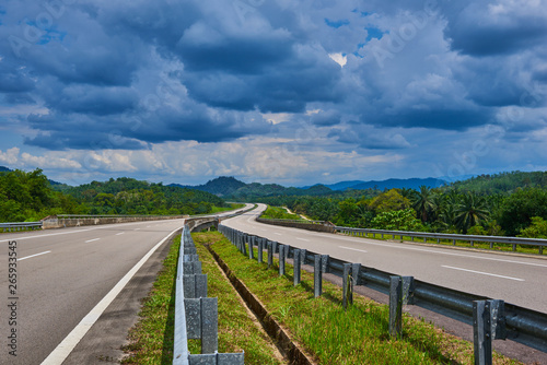 Empty highway or freeway leading to the Cameron Highlands, Malaysia. Spectacular view of the hilly terrain in a blue haze with a cloudy sky and lush tropical rainforest.