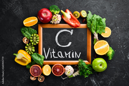 Fruits and vegetables that contain vitamin C: Orange, lemon, apple, roses, garlic, broccoli, apple, kiwi, spinach. Top view. On a black stone background.