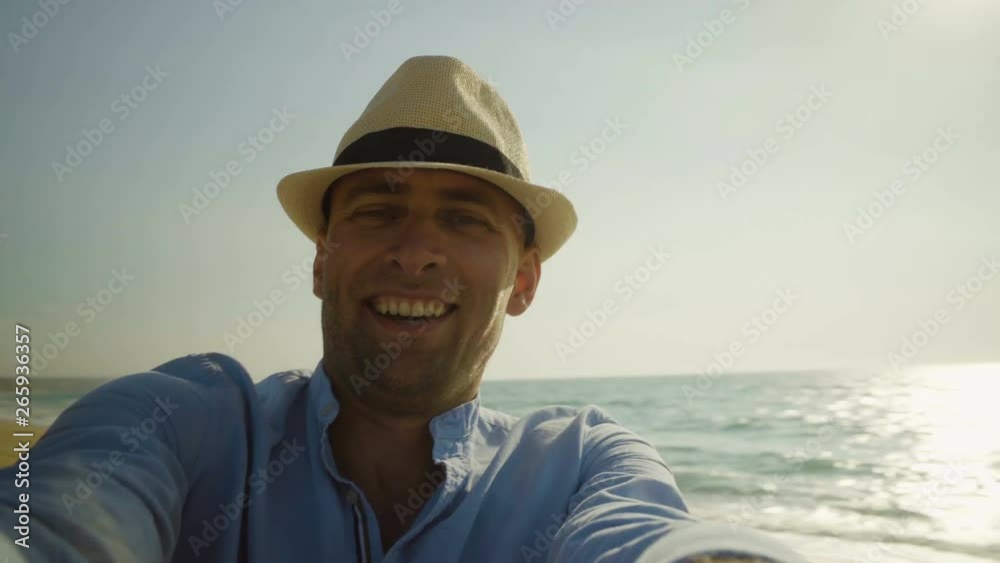 Handsome man in hat turning around on beach. Cheerful young man laughing and smiling at camera while having fun on sandy beach. Emotion concept Handsome man in hat turning around on beach. Cheerful young man laughing and smiling at camera while having fun on sandy beach. Emotion concept