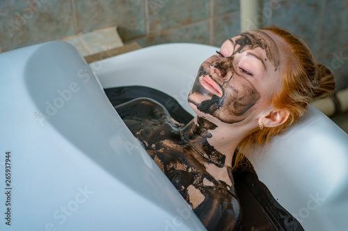 Young woman enjoying mud bath alternative therapy. Woman lies in the bathroom with mud, spa treatments and health.