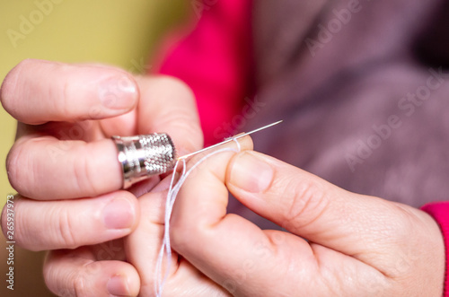 A hand with thimble knotting and cutting a thread on a needle in a sewing session