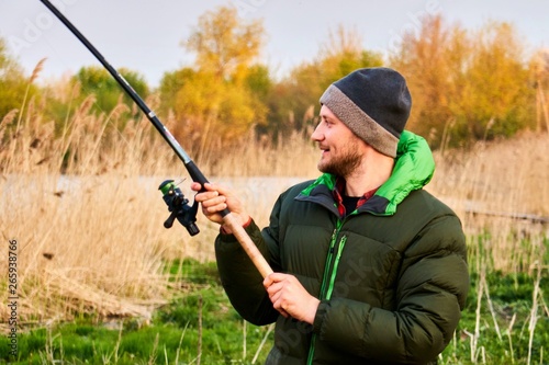 a guy on a spring fishing in a down jacket holds a tight fishing rod