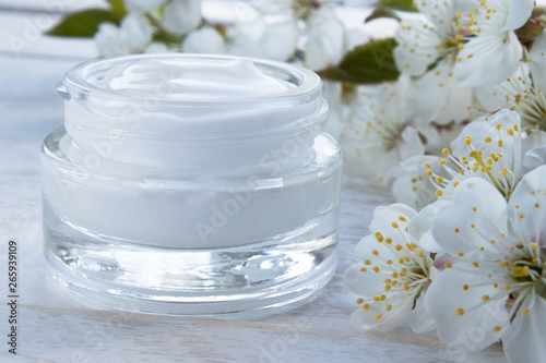 A jar of cream close-up, face cream surrounded by cherry flowers.