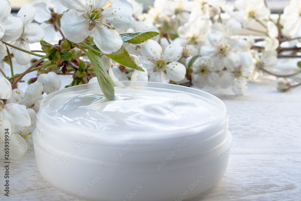 White can, cosmetic cream and cherry flowers on a white background.