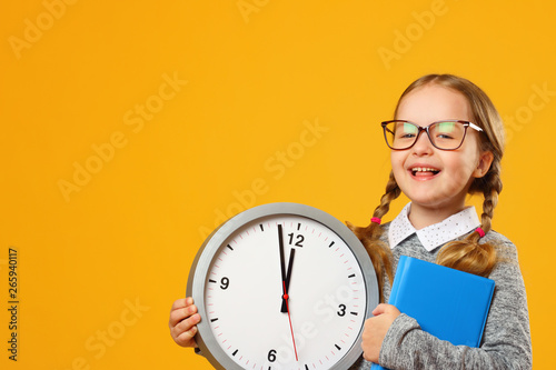 Little girl schoolgirl holds a big clock on a yellow background. The concept of education, development, school, time to learn.