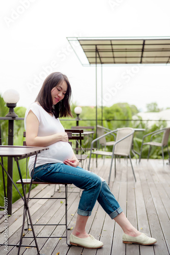 A pretty Asian woman is pregnant. Wearing a white shirt Sit back and relax in the balcony of the house happily.