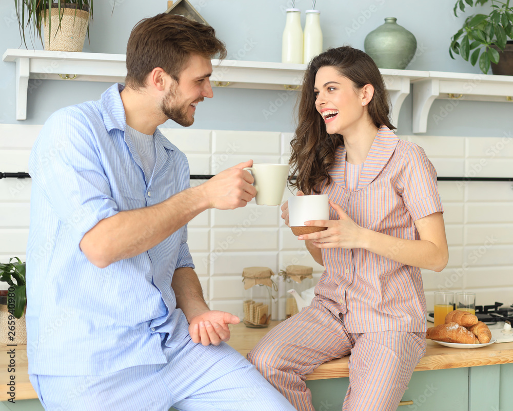 Beautiful young couple in pajamas is looking at each other and smiling while cooking in kitchen at home.