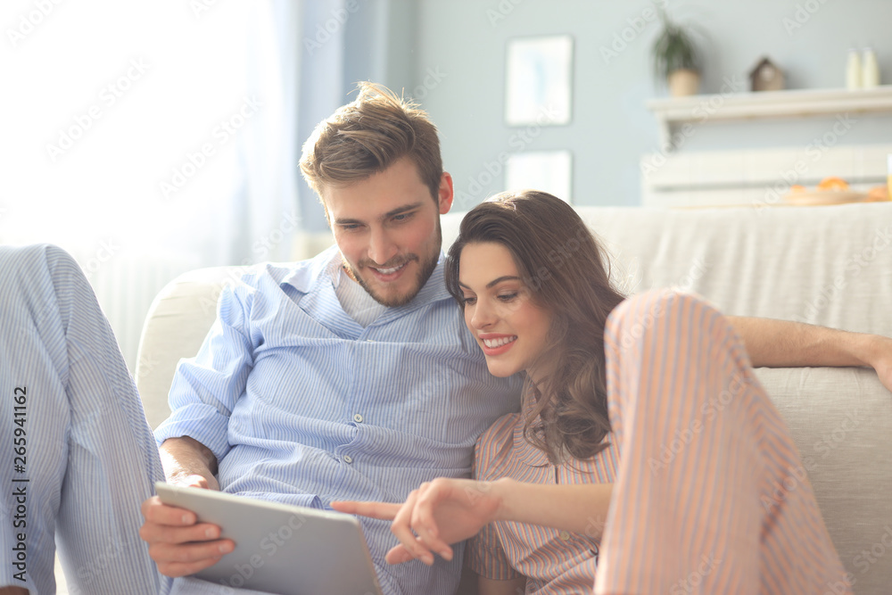 Young couple in pajamas watching media content online in a tablet sitting on the floor in the living room. Young couple in pajamas watching media content online in a tablet sitting on the floor in the living room.