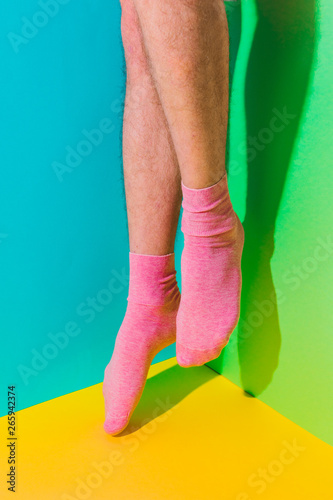 Male feet with hairy skin in socks flying and dancing in the air above bold background in the corner with strong shadows. Minimal art concept. Body part
