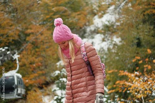 Portrait of beautiful blond girl posing for photo at winter mountain with yellow leaves