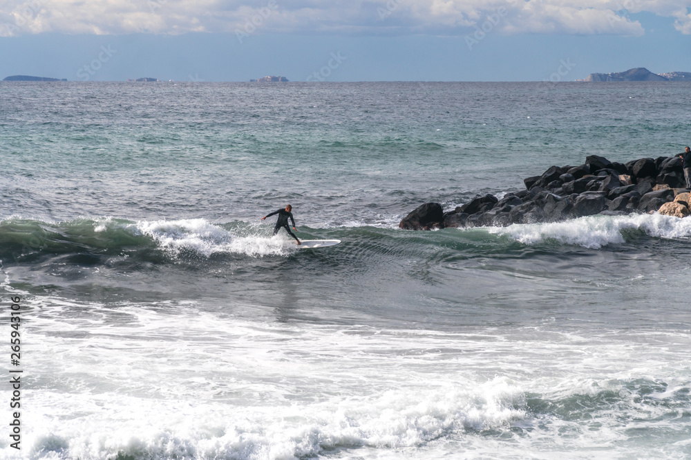 Fototapeta premium The surfer takes a wave, on a surfboard, slides along the wave, in the background of the mountain, Sorrento Italy