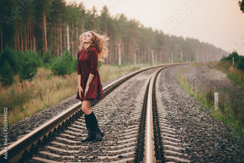 Beautiful dancing girl with curly natural hair enjoy nature in forest on railway. Dreamer lady in burgundy dress walk on railroad. Dance of inspired girl with hair explosion. Sun in hair in autumn.