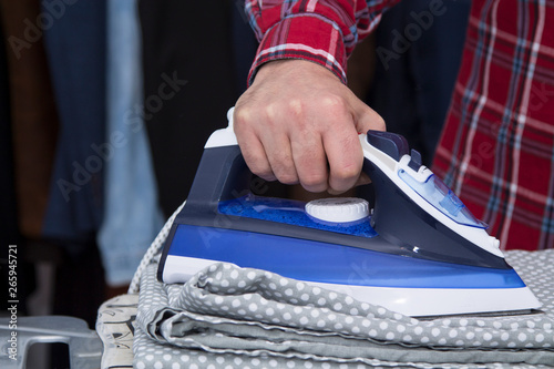 Man irons clothes on ironing board with blue iron. Housework and household concept