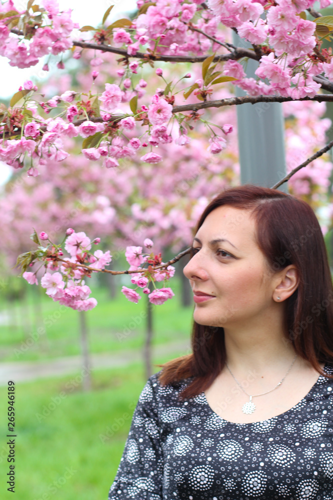Young beautiful girl with long blond hair enjoys the beauty of spring nature near the blossoming sakura tree Young beautiful girl with long blond hair enjoys the beauty of spring nature near the blossoming sakura tree