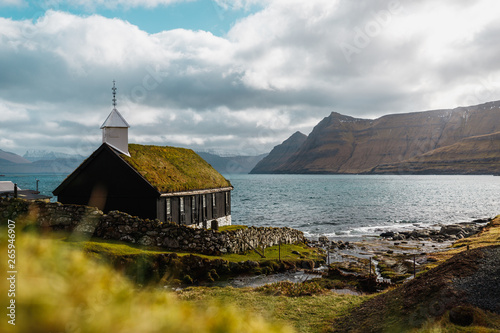 The small picturesque black wooden church of Funningur (Funnings Kirkja) during a sunny spring day with dramatic clouds (Faroe Islands, Denmark, Europe) photo