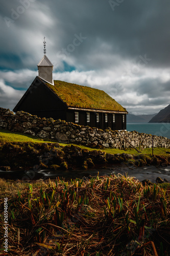 Long exposure of the small picturesque black wooden church of Funningur (Funnings Kirkja) with dramatic clouds and sun (Faroe Islands, Denmark, Europe) photo