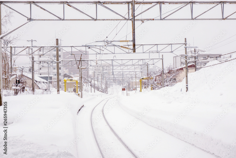 Cityscape view and closeup metal long railroad track in winter season and snow capped city with fully white foggy from snow storm background.