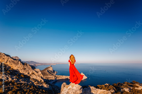 Young beautiful woman in red dress looking to mountains sea. Girl on the nature on blue sky background. Fashion photo © Oleg Gekman