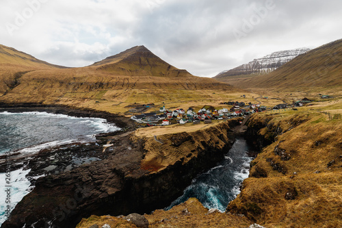 Panoramic view onto the gorge / natural harbour in Gjógv with waves hitting the cliffs and the sun in the background (Faroe Islands, Denmark, Europe)