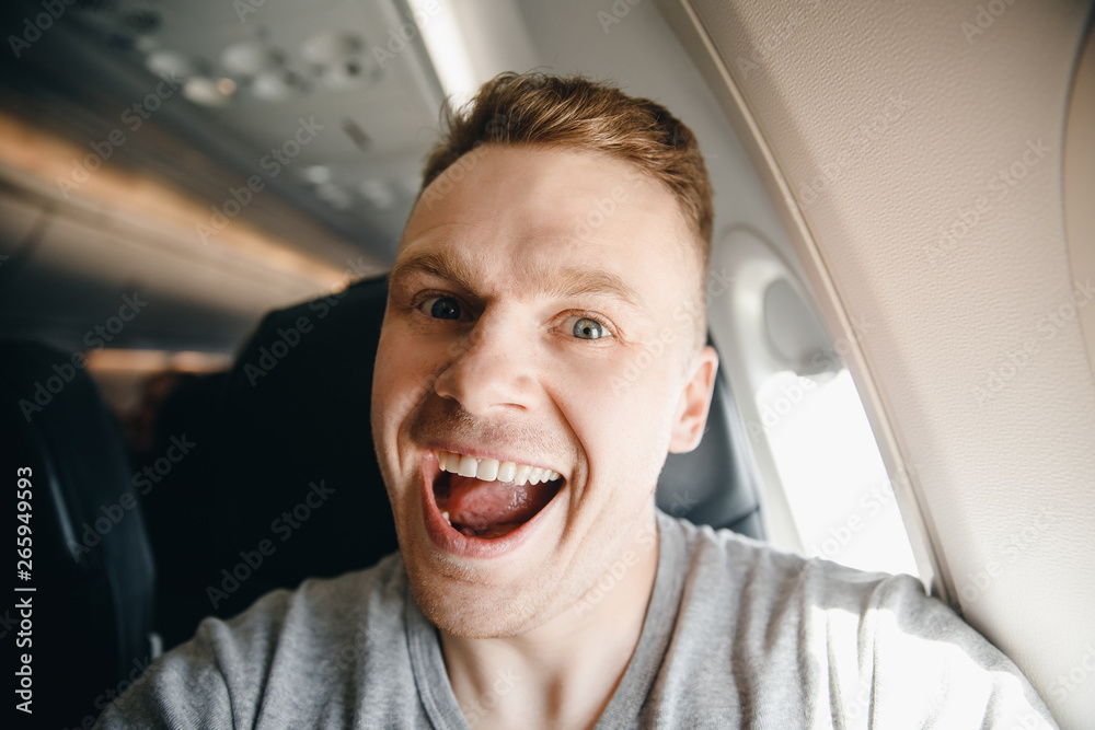 Happy tourist man makes selfie photo in cabin aircraft airplane before departure. Travel concept