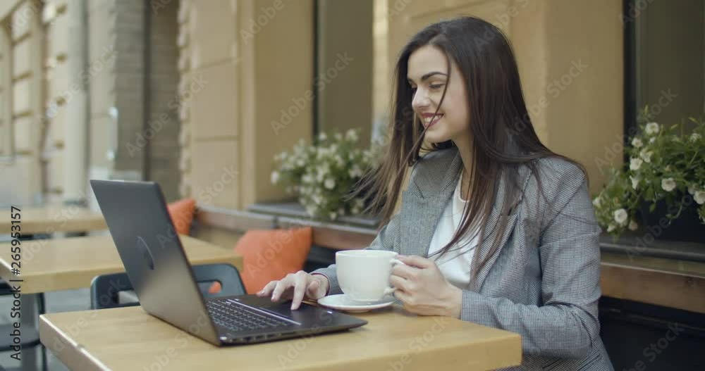 Pretty student girl using laptop in outdoors cafe while having cup of coffee Pretty student girl using laptop in outdoors cafe while having cup of coffee