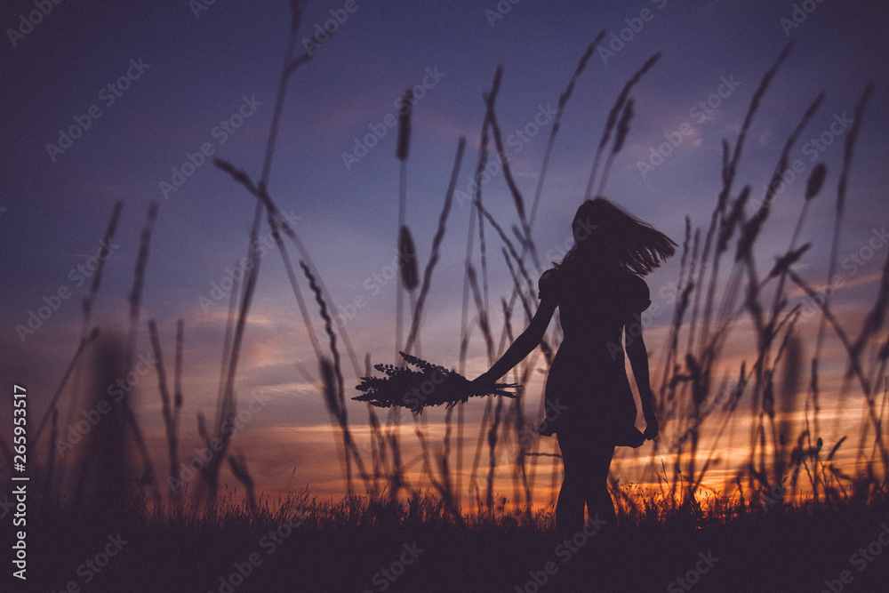 Silhouette of a beautiful girl holding a bunch of flowers at a meadow on the background of the sunset