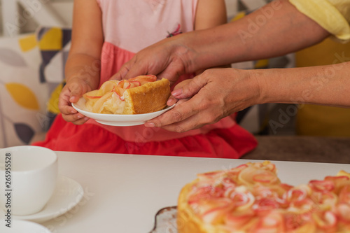 Enjoying holidays together. Senior woman in kitchen with her granddaughter. They are holding baked apple pie. Woman treating her granddaughter by self-baked pie.