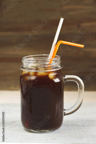 coffee beverage cold brew drink with ice and two tubules on a white wooden table top in a glass mug jar with a handle with a back wooden background in rustic style