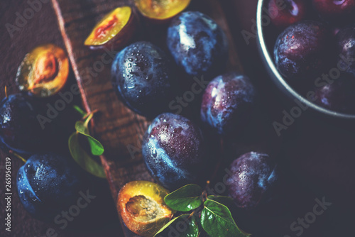 Fresh ripe plums with leaves on a brown wooden board. Top view, toned image. Selective focus.