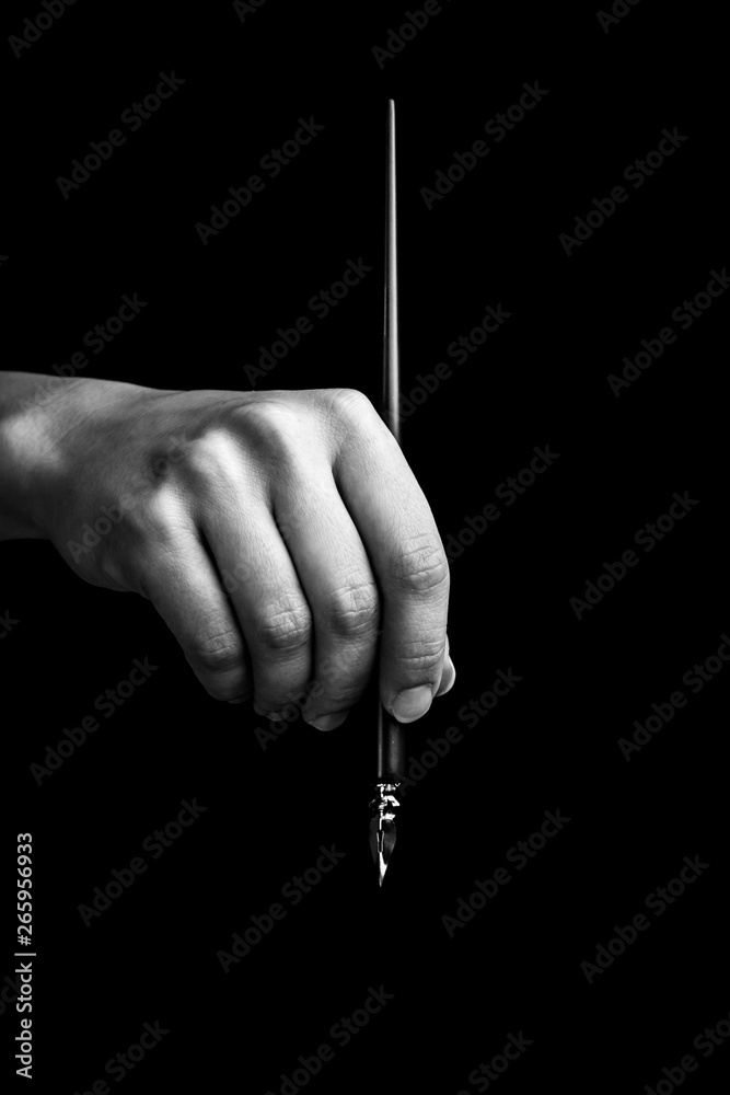 female hand elegantly holding an ink pen with a metal tip close-up on a black background. classic fountain pen isolated macro black and white. copy space. vertical - obrazy, fototapety, plakaty 