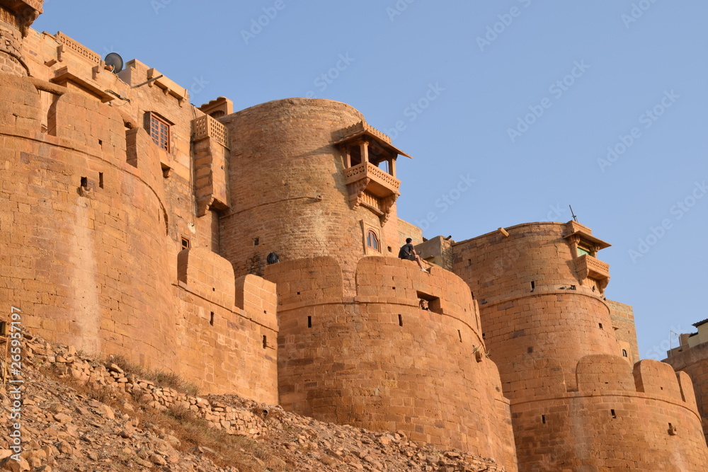 Wall of Jaisalmer fort with indian people sitting on top by sunset, taken in Jaisalmer India in the state Rajasthan
