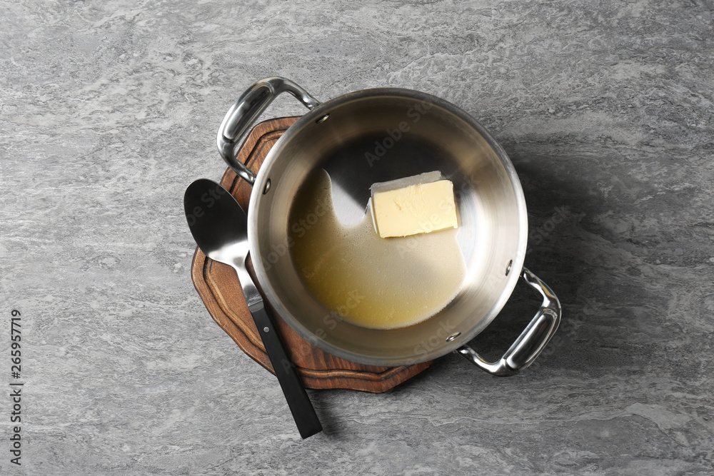 Pot with melting butter and spoon on grey background, top view