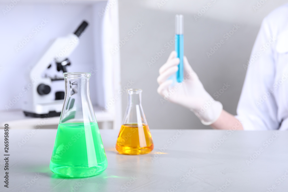 Glassware with samples on table and assistant in chemistry laboratory Glassware with samples on table and assistant in chemistry laboratory