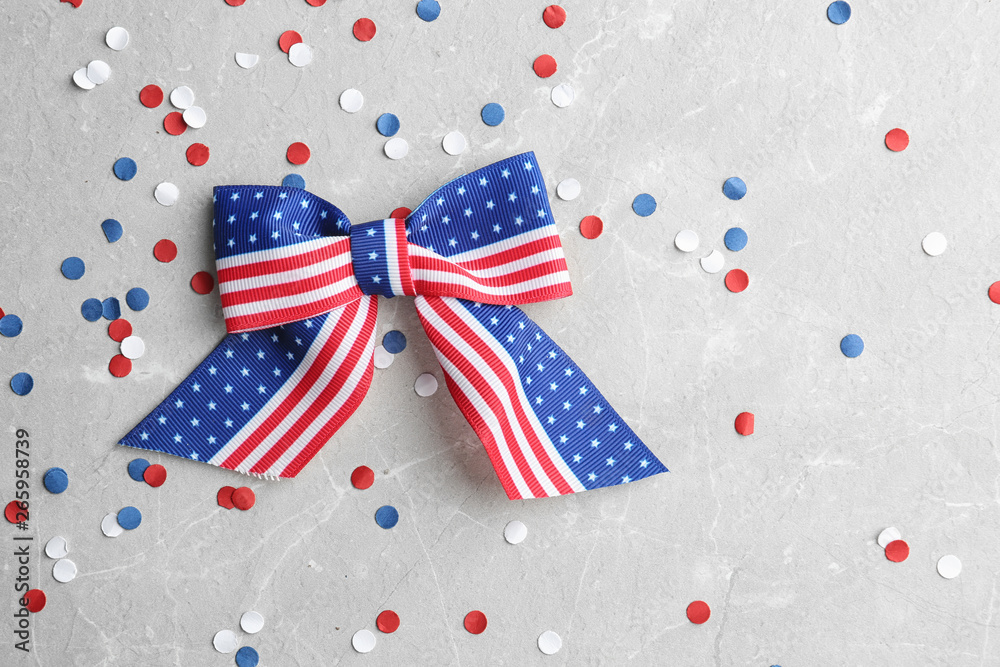 Obraz premium Ribbon bow with American flag pattern and confetti on light background, flat lay with space for text. USA Independence Day