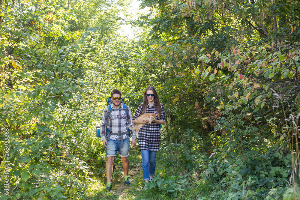 Obraz premium Travel, adventures, hike, tourism and nature concept - Tourist couple with cat walking in the woods