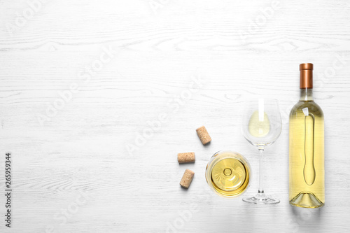 Glasses and bottle with white wine on wooden background, flat lay. Space for text photo