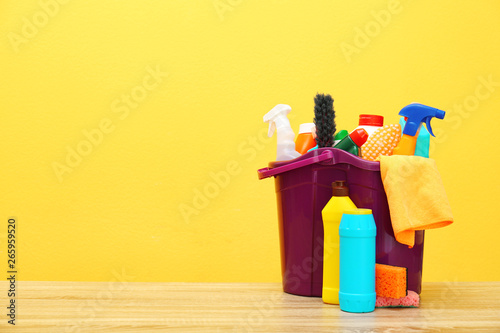 Bucket with cleaning supplies on wooden table against color background. Space for text