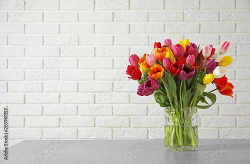 Vase with beautiful spring tulip flowers on table near brick wall. Space for text