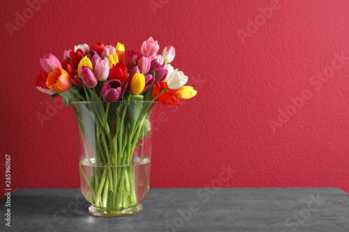 Vase with beautiful spring tulip flowers on color background. Space for text