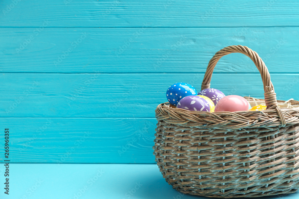 Wicker basket with painted Easter eggs on table against wooden background, space for text Wicker basket with painted Easter eggs on table against wooden background, space for text